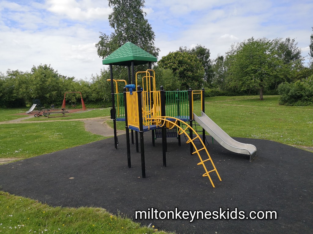 Green and yellow climbing frame with a slide on tarmac