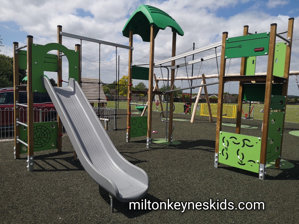 Green and metal climbing frame with a slide in the play area in North Crawley 